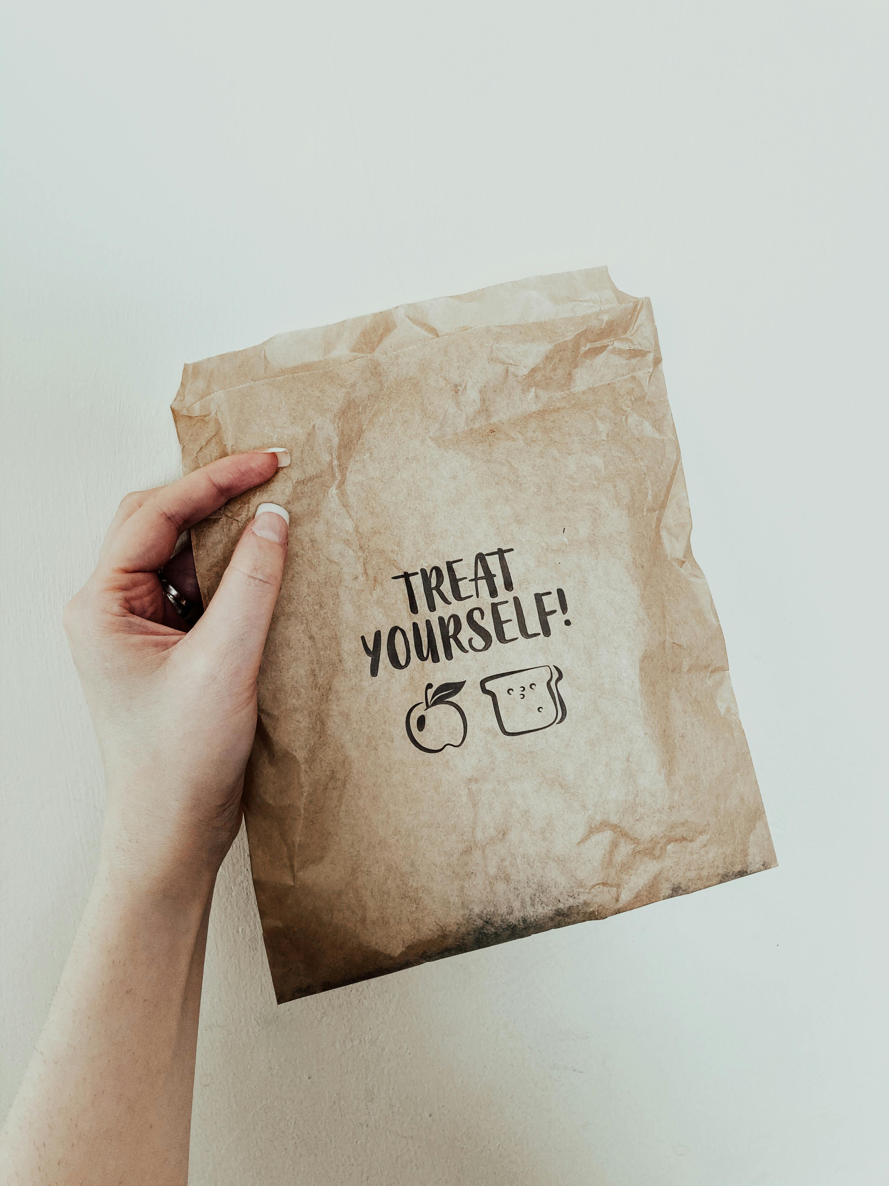 crop faceless woman showing paper bag against white wall