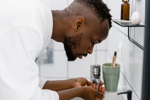Free A man engaged in self-care, washing hands at a sink, in a modern bathroom. Stock Photo
