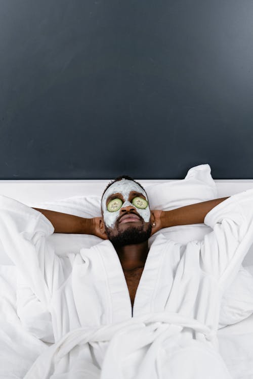 A Man in White Robe Lying Down while Relaxing on His Bed