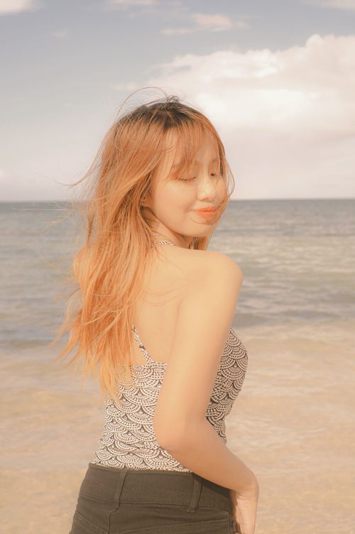 Free Young woman posing by the beach, enjoying a sunny day with waves in the background. Stock Photo