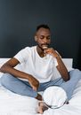 Man in White Crew Neck T-shirt and Blue Denim Jeans Sitting on Bed