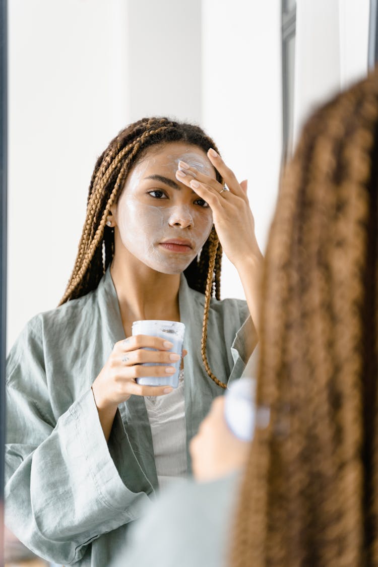 A Woman Applying A Cream On Her Face While Looking At The Mirror