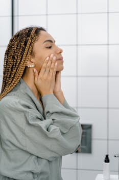 Woman with braided hair applying skincare in a bathroom setting.