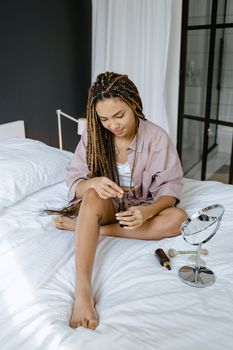 A woman with braided hair sitting on a bed, holding a bottle, emphasizing self-care and relaxation.