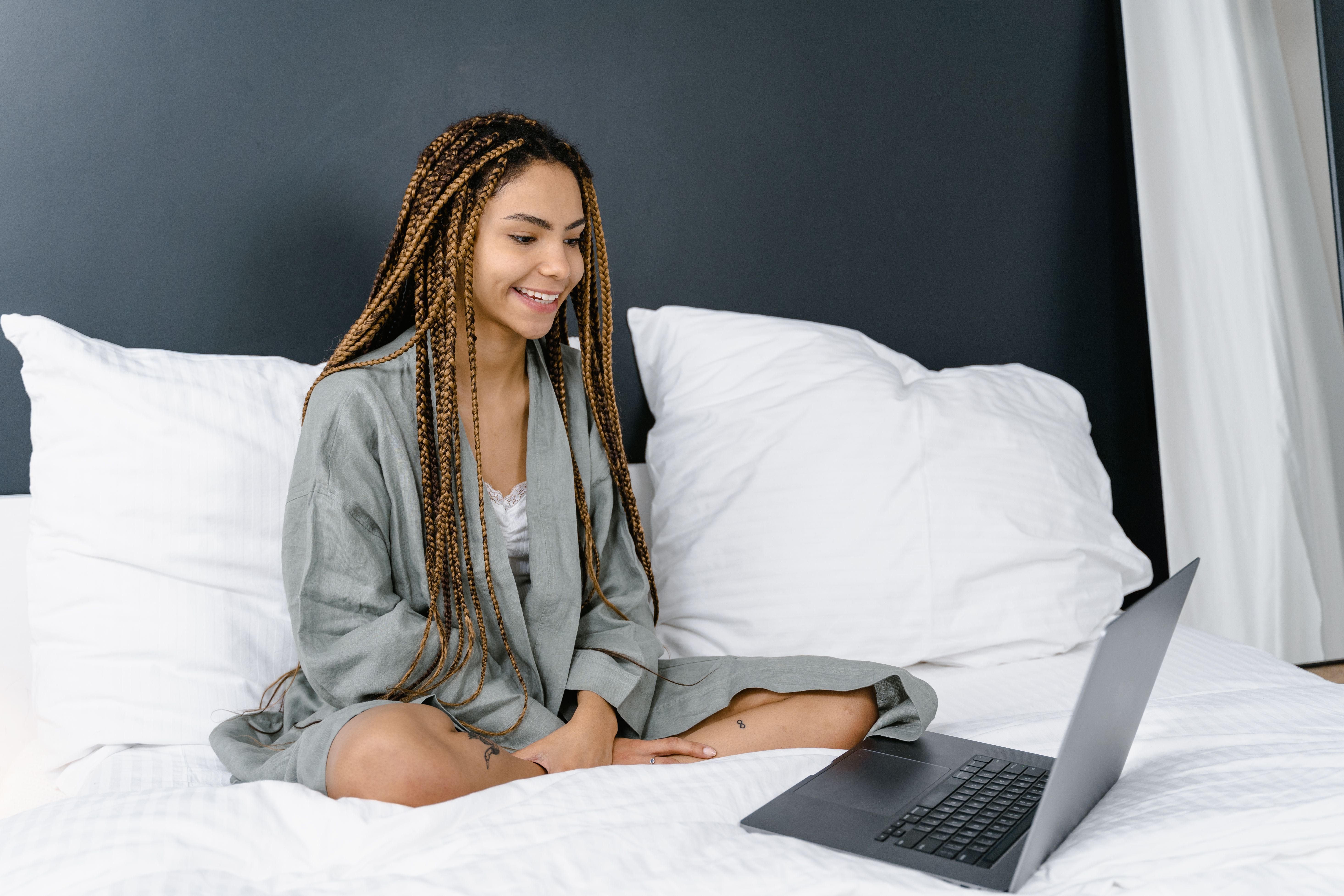 Smiling young woman sitting on a bed in a bathrobe in front of an open laptop