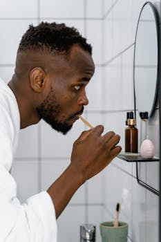 African man brushing teeth, promoting oral hygiene in a modern bathroom setting.
