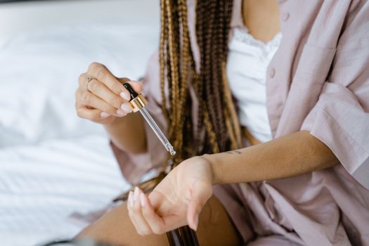 Close-up of a woman applying essential oil to her skin using a dropper for skincare.
