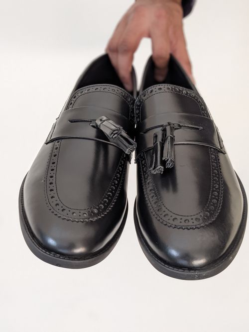 Free Close-up of black leather loafers with tassels held by a hand. Stock Photo