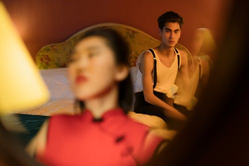 Free Man Sitting on the Bed Looking at the Woman in Front of the Mirror Stock Photo