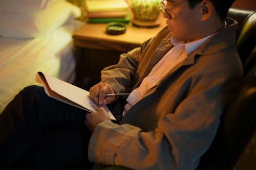 Free A Man Sitting on a Chair while Holding a Pen and Notebook Stock Photo