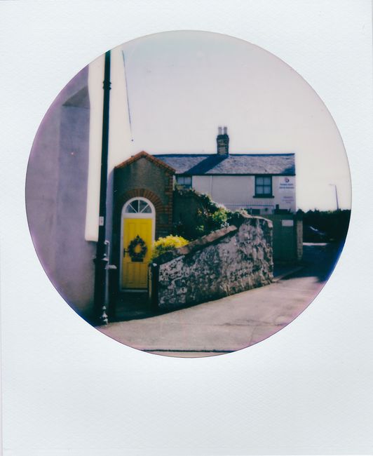 Retro photograph of a quaint village house with a vibrant yellow door and rustic stone walls.