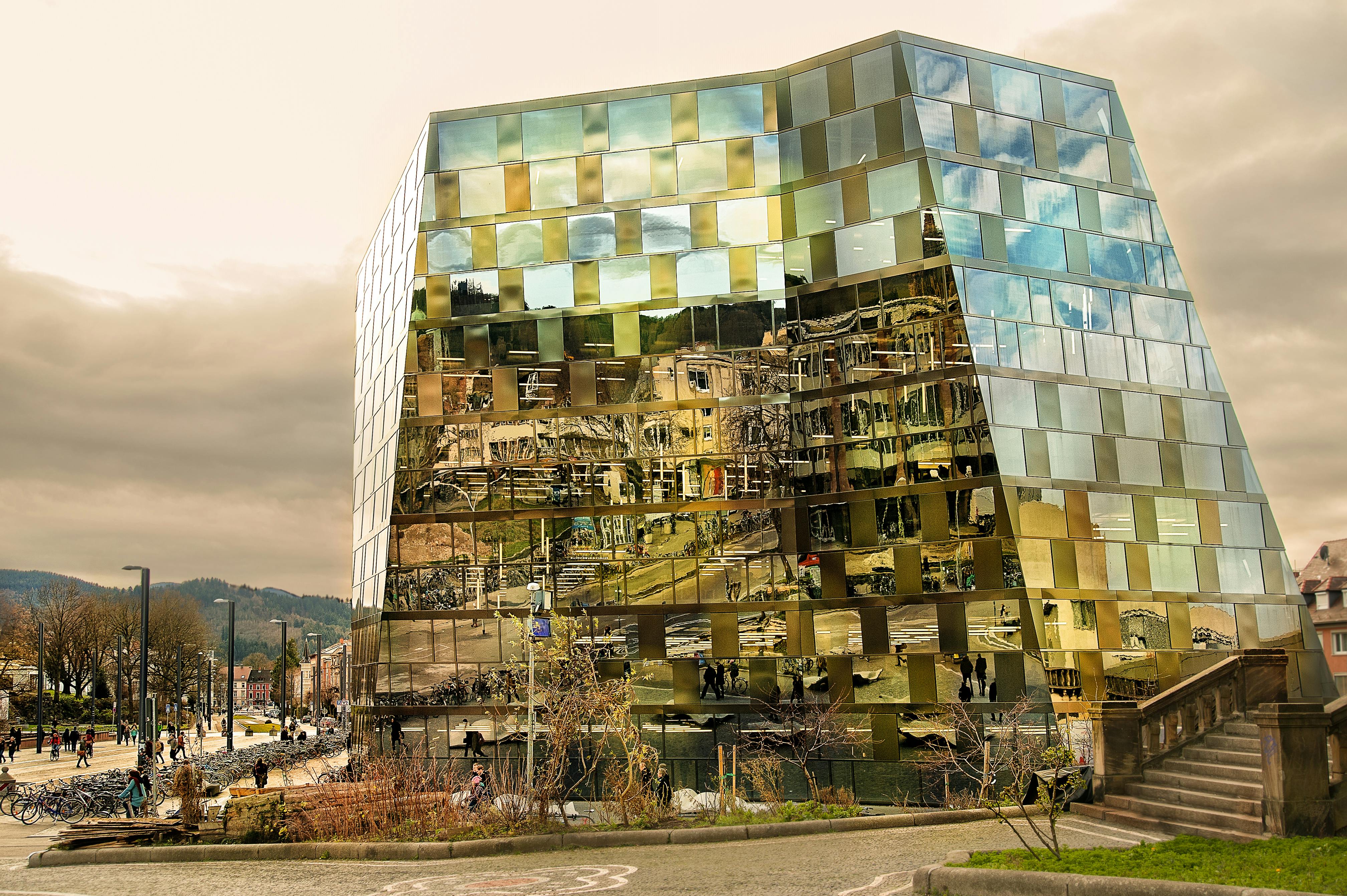 一座现代玻璃建筑倒映出城市环境和多云的天空