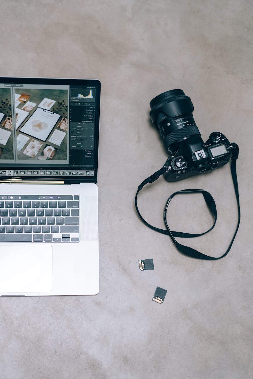 A creative flat lay featuring a laptop, DSLR camera, and memory cards on a neutral surface.