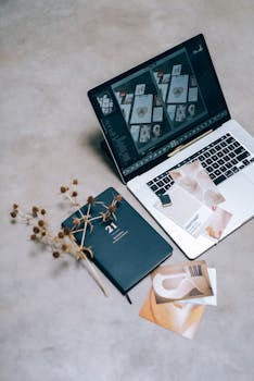 A high-angle shot of a creative workspace featuring a laptop, planner, and dried flowers on a flat surface.