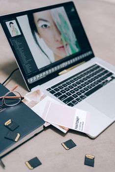 A workspace with a laptop displaying editing software, memory cards, and Pantone color guide.