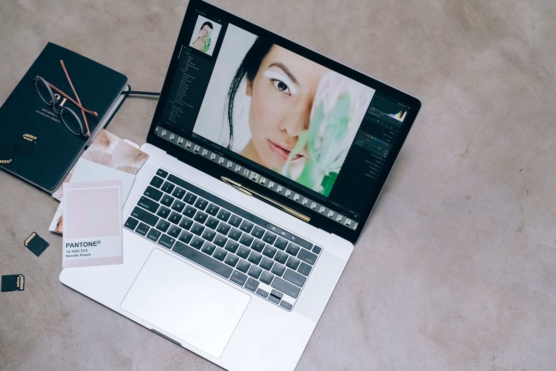High-angle view of a creative workspace with a laptop, eyeglasses, and photography editing elements.