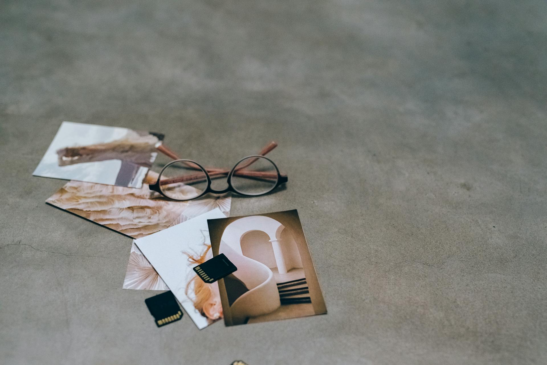 Black Framed Eyeglasses and Memory Cards Beside Scattered Photos