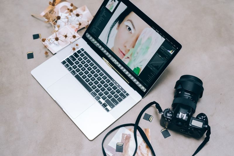 Flat lay of a laptop with photo-editing software open, camera and design tools on a desk