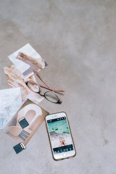 A stylish flat lay on a concrete background featuring a smartphone, eyeglasses, and printed photos.