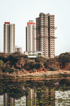 High-rise residential towers reflected in a calm lakeside setting during the day.