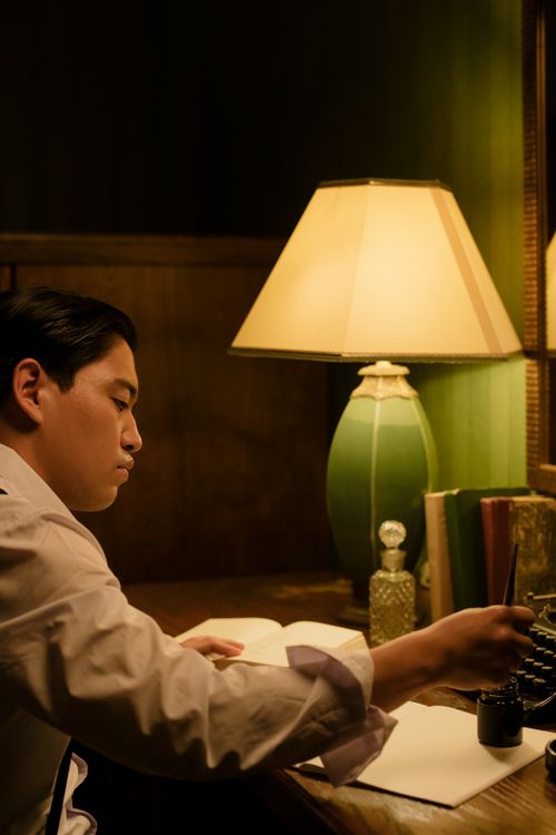 Free A man deeply focused on writing at a desk under the warm glow of a vintage lamp. Stock Photo