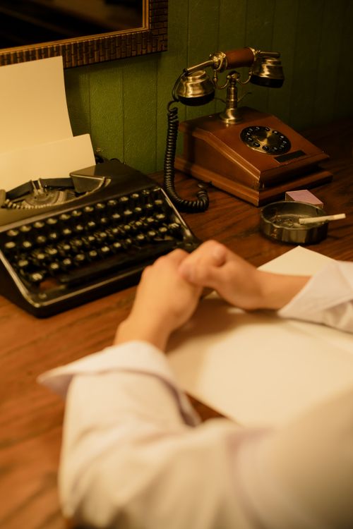 Free A retro office scene featuring an old typewriter, rotary phone, and a person at a desk. Stock Photo