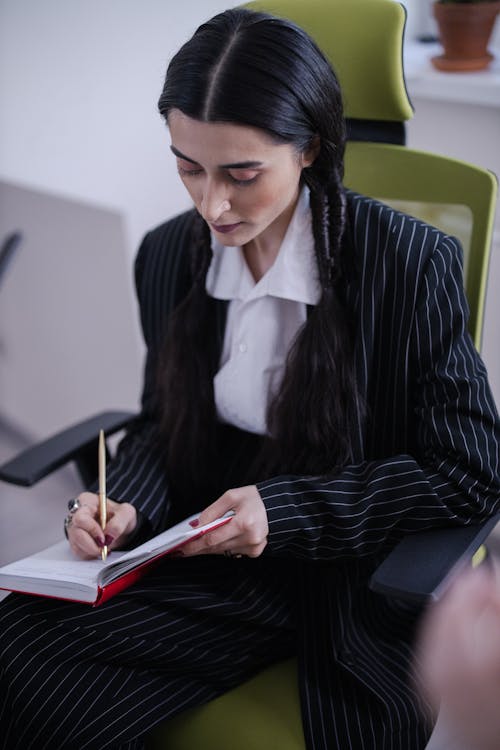 A Woman in Black Blazer Sitting while Taking Notes