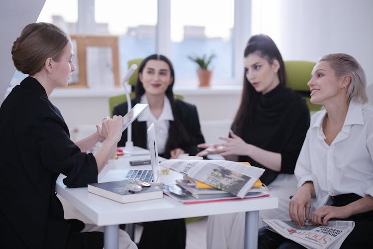 A Woman In Black Blazer Holding A Tablet While Talking To The People In Front Of Her