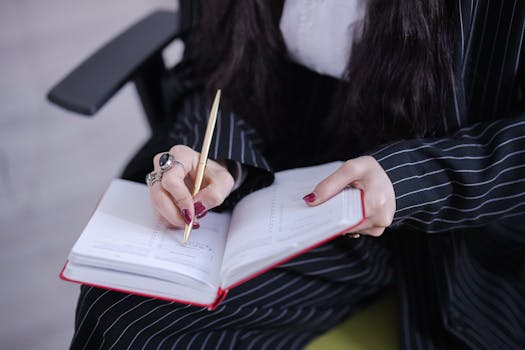 A woman in a pinstripe suit writing notes in a planner with a gold pen.