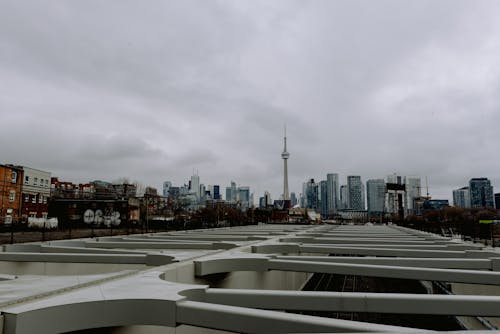 Free Modern tall observation tower located in distance near contemporary skyscrapers and residential buildings on street with metal structure against cloudy sky in Toronto Stock Photo
