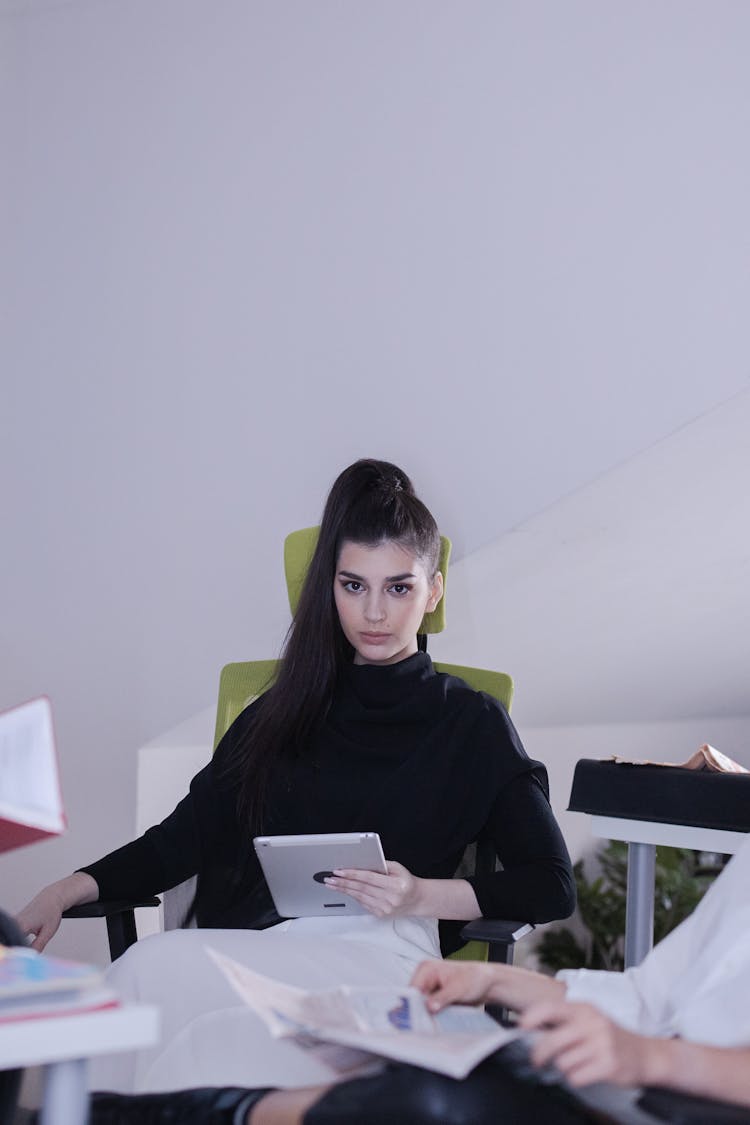 A Beautiful Woman In Black Turtleneck Sweater Sitting On The Chair While Holding A Tablet