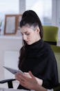 A Woman in Black Long Sleeves Sitting while Holding a Tablet