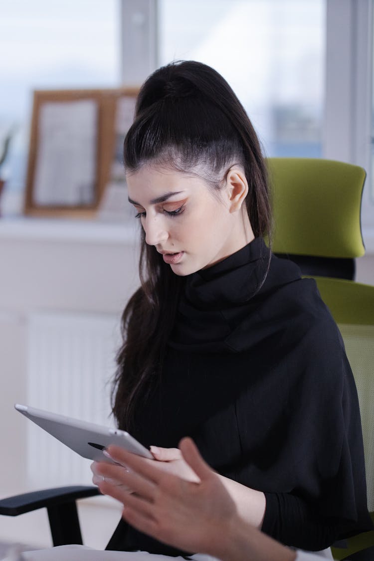 A Woman In Black Long Sleeves Sitting While Holding A Tablet