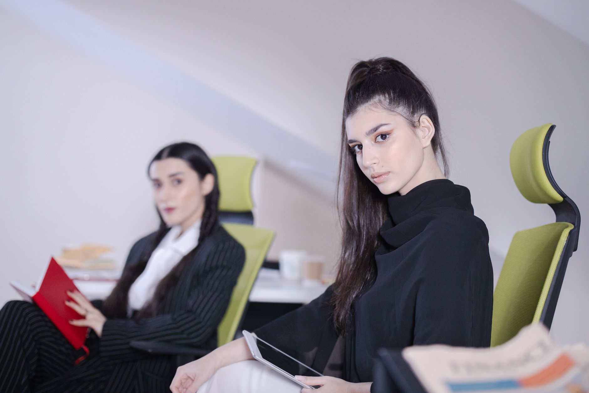 Two businesswomen sitting in a modern office with technology, engaged in work.