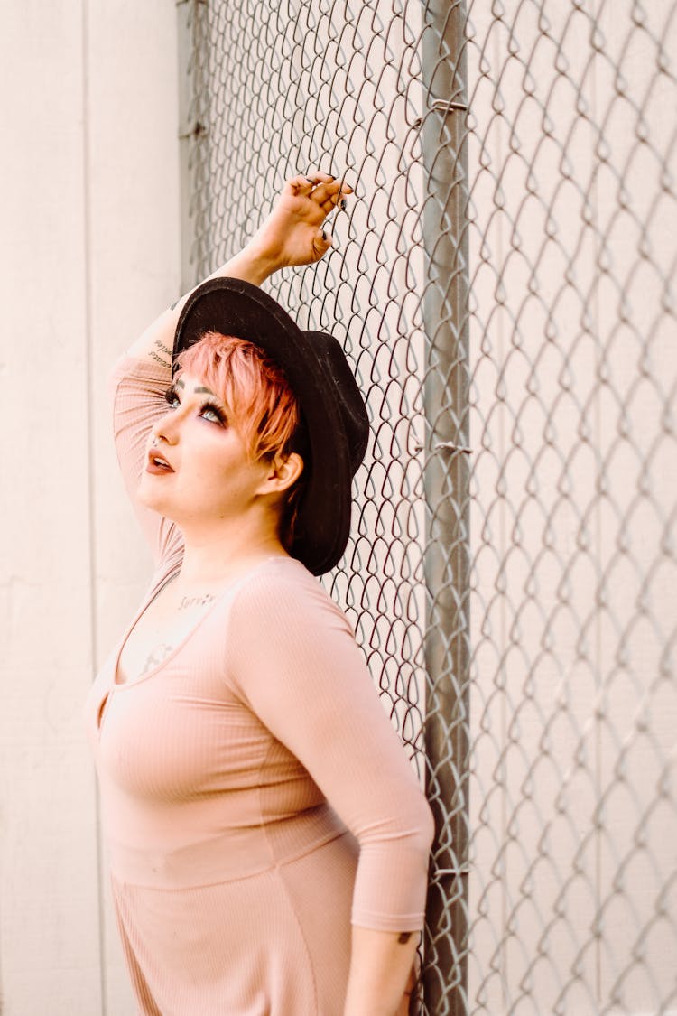 Trendy Model With Makeup In Hat Against Grid Fence