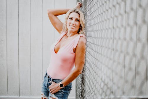 Free Cheerful adult blond female in trendy wear and wearable tracker looking at camera while leaning on grid fence Stock Photo