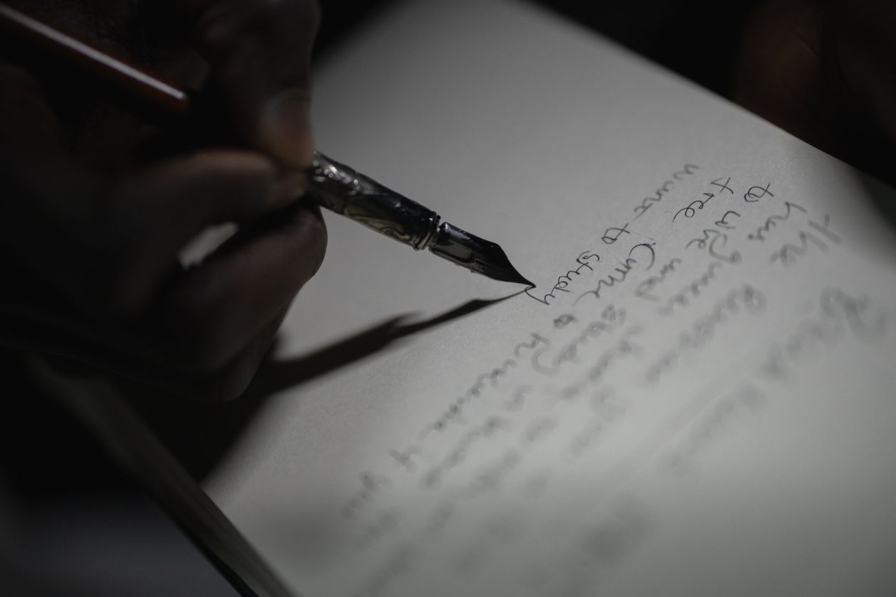A person's hand writing gracefully on paper with a dark fountain pen — fountain pen journaling