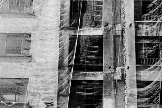 Abstract grayscale photo of a building facade covered with a mesh net during construction.