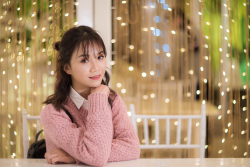 Free Beautiful young woman in a pink sweater posing in front of a sparkling light backdrop. Stock Photo