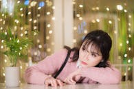 一名穿着粉色毛衣的女子若有所思地凝视着一家灯光柔和、氛围舒适的咖啡馆