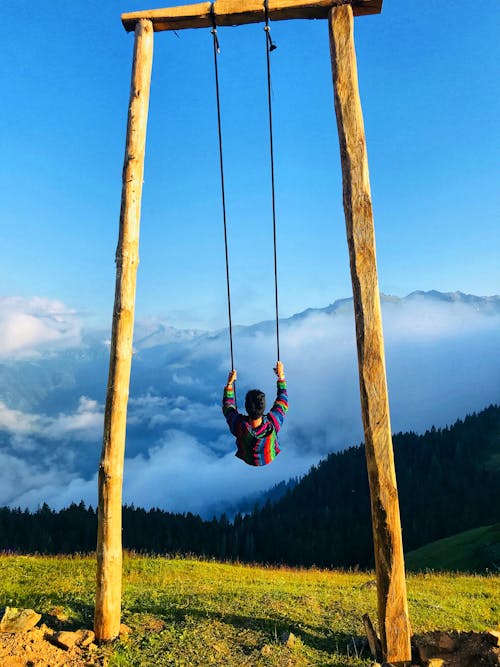 A Man Sitting on Swing Under the Blue Sky