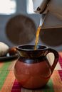Steaming hot bouillon pouring into rustic clay jug placed on table for meal