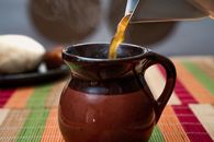 Hot broth pouring from kettle into ceramic jug placed on table in kitchen