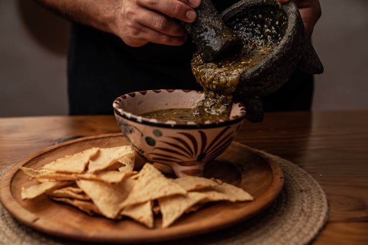 Person Pouring Salsa In A Ceramic Bowl