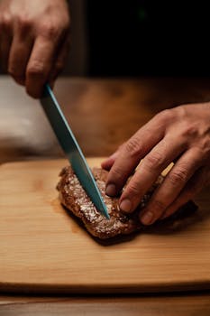 Close-up of hands slicing a juicy steak on a wooden cutting board, showcasing food preparation.