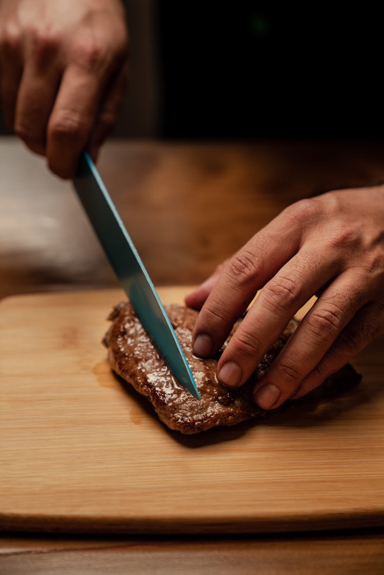 Person Slicing Meat On Brown Chopping Board