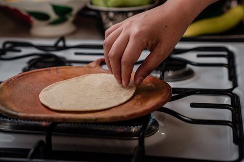 Free A hand placing a tortilla on a clay comal on a stove, preparing traditional Mexican food. Stock Photo