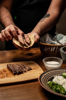 Close-up of hands preparing a steak taco with fresh ingredients on a wooden board.