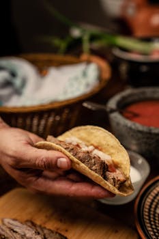 Close-up of a hand holding an authentic Mexican taco with fresh ingredients, highlighting traditional flavors.