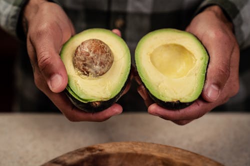 High angle of crop anonymous male demonstrating ripe halved avocado while standing at table